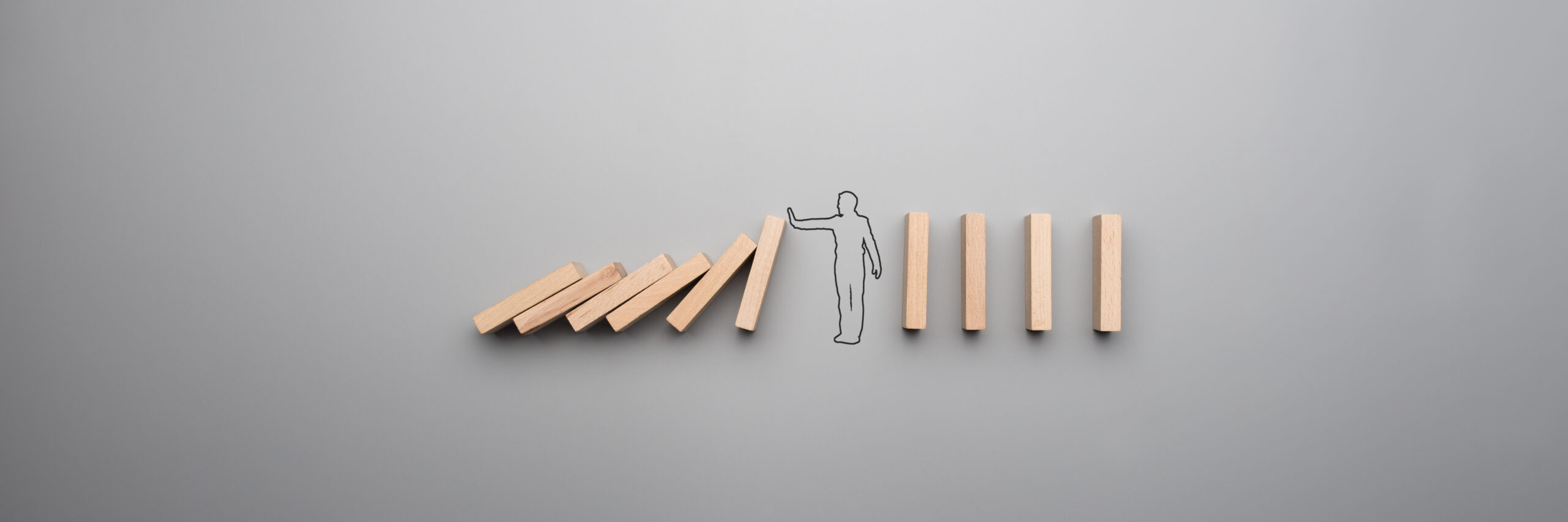 Wide cropped image of the outline of a businessman stopping the domino effect on gray background.